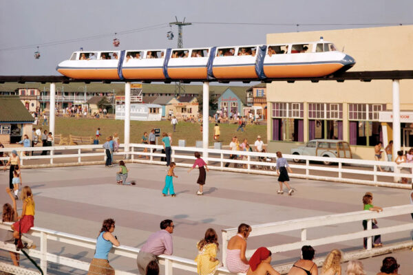 Train vehicle moving on an ariel track above an outdoor rollerblading rink