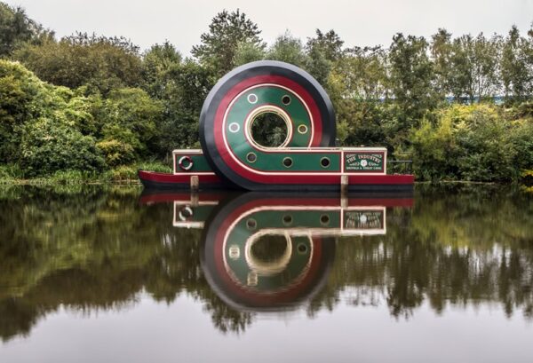 A canal boat on a canal. The structure of the boat is morphed and has a full loop in its structure.