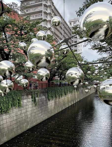Mirrored kinetic balls floating above a canal.