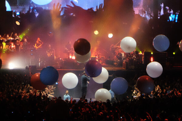 Singer performing on stage as colourful balloons fall from the ceiling.