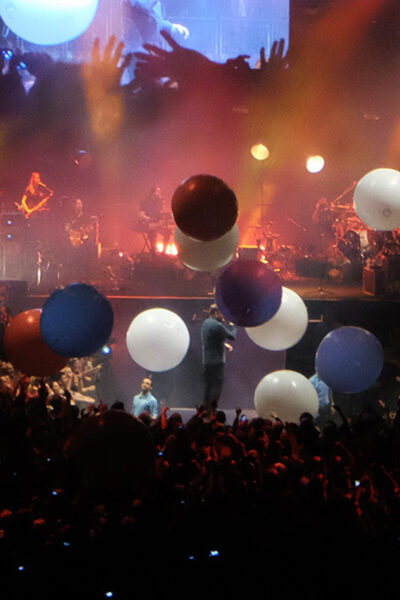 Singer performing on stage as colourful balloons fall from the ceiling.