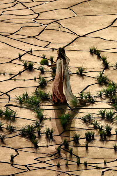 Woman walking on a stage as a trail of kinetic grass rises behind her.