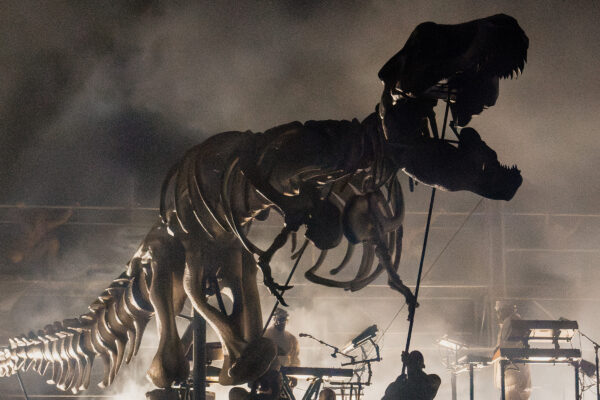 Large T-Rex puppet emerging onto a stage surrounded by a cloud of haze.