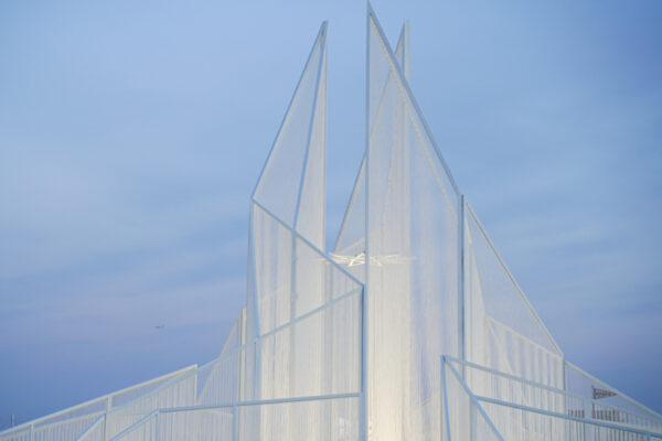A white pointed art structure in front of a blue sky.
