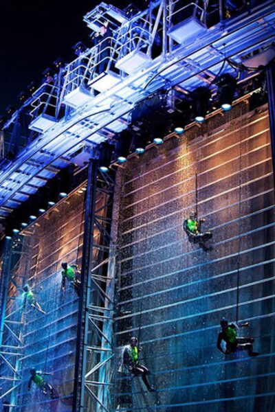 People climbing down a vertical water wall as a part of a stage design.