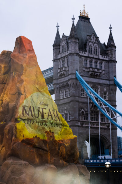 Shot of scenic rock build in front of Tower Bridge. Mufasa's film branding is projected onto the rock.