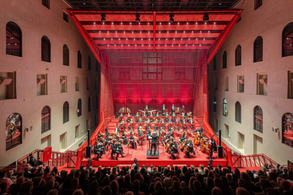 An orchestra performing on a red stage structure that is in the middle of an older building