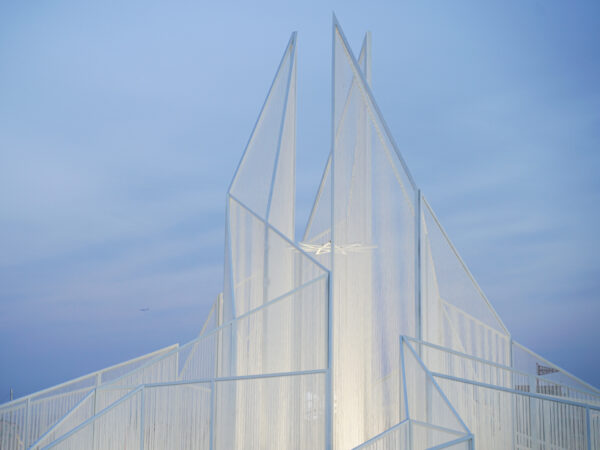 A white pointed art structure in front of a blue sky.