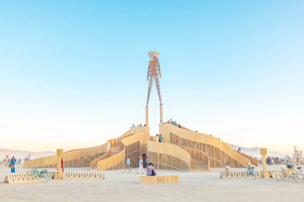A wooden installation made up of staircases and a tall person-like structure in the desert.
