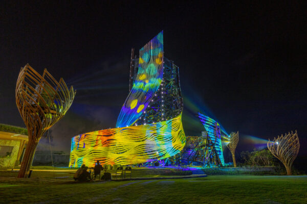 Image of a large wooden, swooping structure with colourful projections being projected onto it.